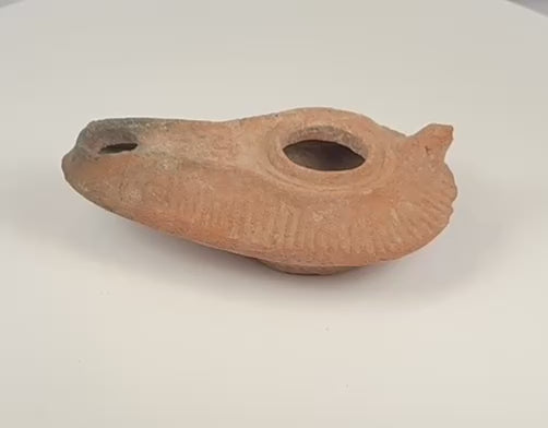 Rotating view of a Late Antique to Early Islamic mould-made terracotta oil lamp with an elongated slipper-shaped body, central filling aperture, extended wick nozzle, radiating grooves, partial rear handle, recessed base, mineral deposits, and historic soot staining