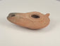 Rotating view of a Late Antique to Early Islamic mould-made terracotta oil lamp with an elongated slipper-shaped body, central filling aperture, extended wick nozzle, radiating grooves, partial rear handle, recessed base, mineral deposits, and historic soot staining