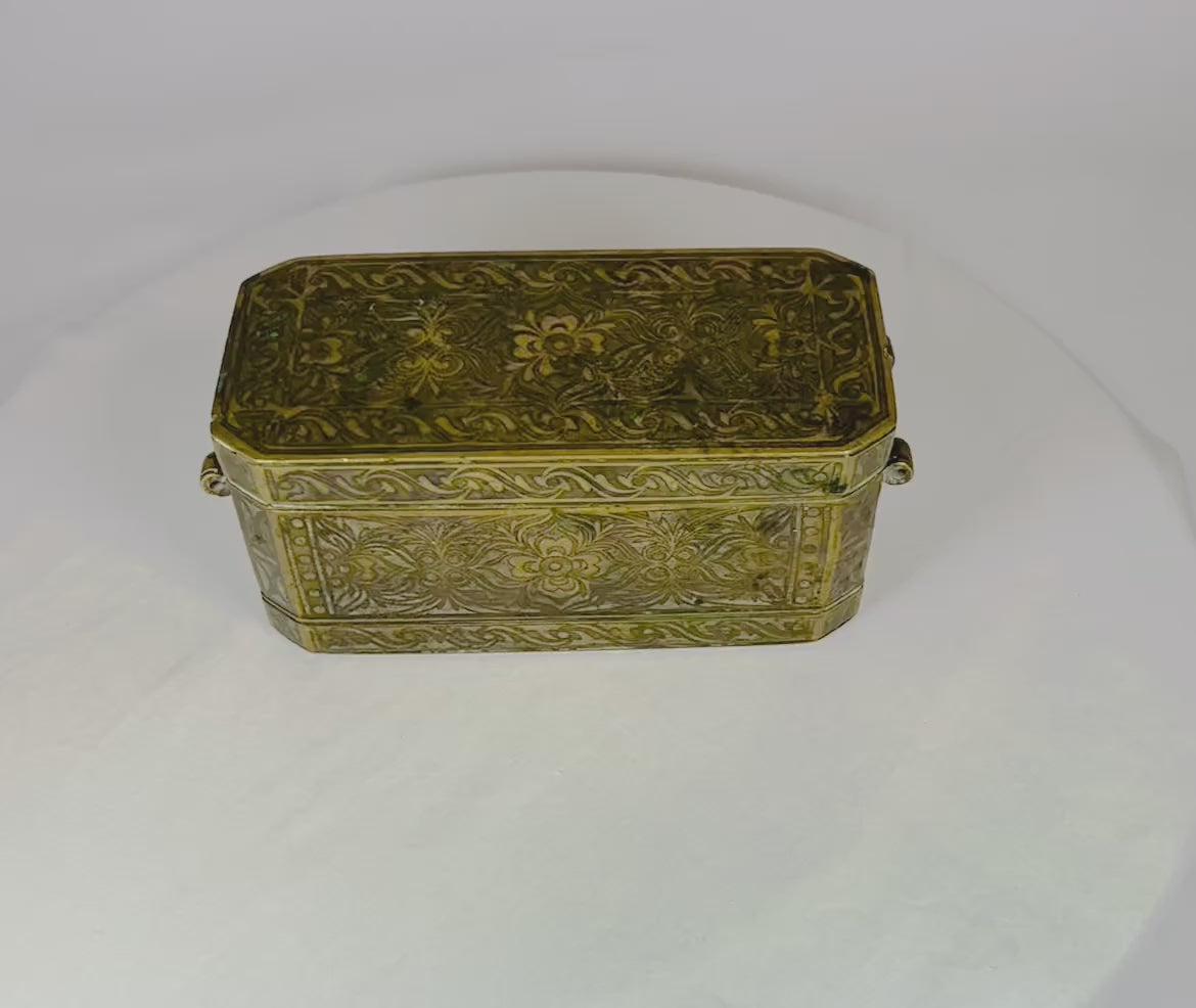 Antique rectangular betel nut box from Mindanao, Philippines, circa 1780–1820. Mixed metal alloy with brass and copper inlay featuring hand-engraved floral motifs, four internal hinged compartments, and side rings for suspension. Reflects Southeast Asian metalworking traditions and ceremonial betel chewing practices.