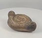 360-degree rotating view of a Roman-style terracotta oil lamp, attributed to circa 100–200 AD, featuring a recessed central discus with an apparent ithyphallic male figure, decorative circular and scrolling motifs, a raised rear handle, and a darkened wick nozzle. The video highlights the lamp’s earthy brown patina, detailed relief decoration, surface wear, and rounded construction from multiple angles.