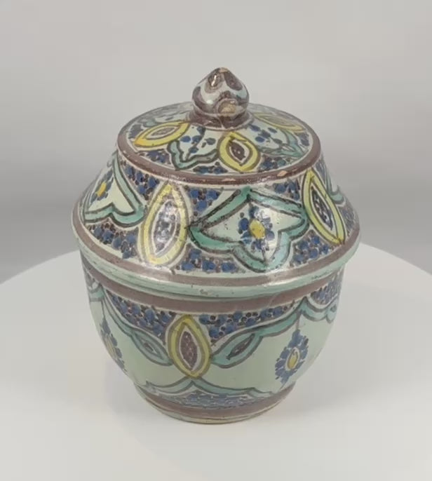 360-degree rotating view of an antique Moroccan hand-painted covered pottery jar from Fes, featuring vibrant polychrome floral decoration, a fitted domed lid, glazed earthenware construction, and traditional Islamic-inspired ornamentation.