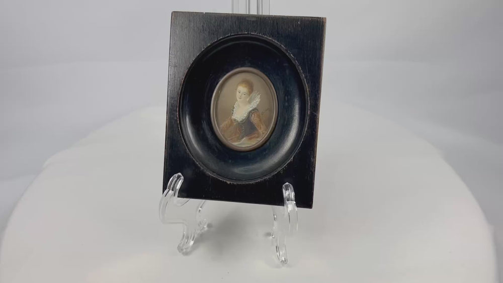 Mid–late 19th-century Continental European miniature portrait of a young woman in historicizing costume with deep blue bodice, amber sleeves, and lace ruff, watercolor/gouache on thin wafer, signed lower right, in ebonized wood frame with oval brass bezel, after Fragonard, circa 1860–1890.