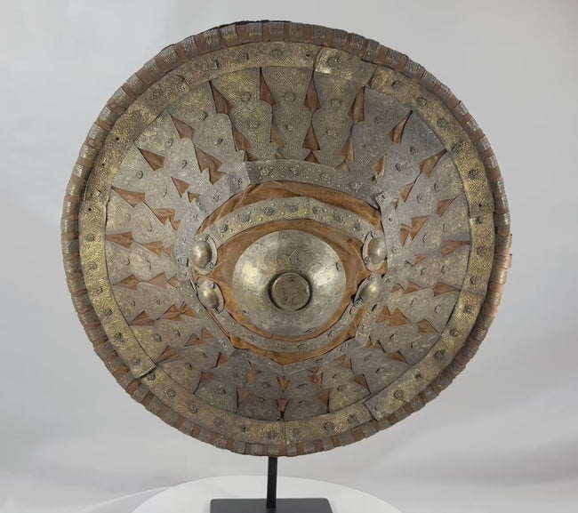 Rotating view of a late 19th-century Ethiopian Ras shield with a convex hide body, golden-brown velvet covering, pierced and engraved silvered and gilt metal mounts, radiating bosses, a large central sunburst boss, red leather reverse, and original padded handgrip