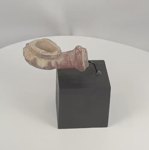 Rotating view of a Late Ottoman terracotta tobacco-pipe bowl with a deep cylindrical chamber, broad raised opening, scalloped petal-shaped border, impressed crosshatched decoration, tubular detachable-stem socket, moulded terminal rings, reddish-purple slip, pale mineral deposits, burial encrustation, edge wear, and a custom curved metal mount on a black wooden display base