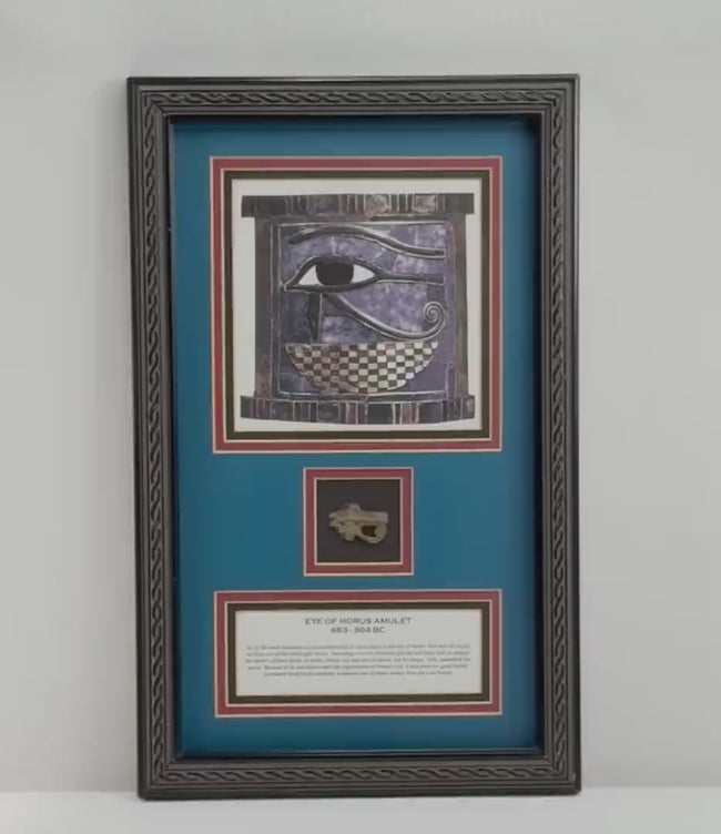 Video of a framed ancient Egyptian Eye of Horus (Wedjat) soapstone amulet attributed to the Late Period, circa 663–304 BCE. The display features an ornate black frame, deep blue background, Egyptian Eye of Horus illustration, and historical identification plaque, with close-up views of the carved stone amulet and its aged surface details.