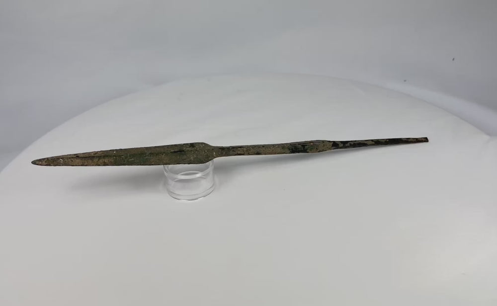 360 video of an ancient Bronze Age spearhead rotating on white display stand, showing patina, form, and tapered blade.