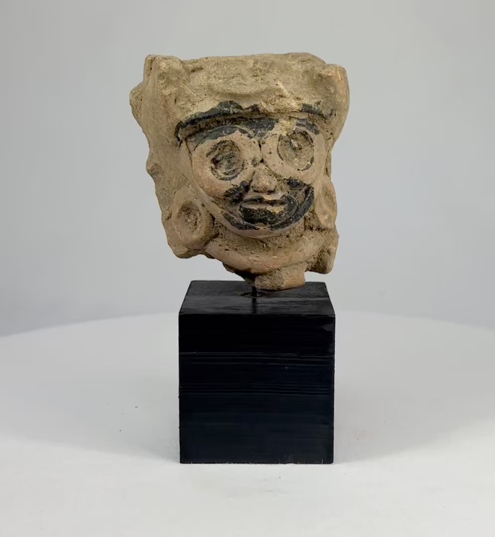 Late Classic Period Mesoamerican ceramic head fragment, circa 500–900 CE, with finely modeled features, large circular earrings, and traces of black pigment, mounted on a display stand.