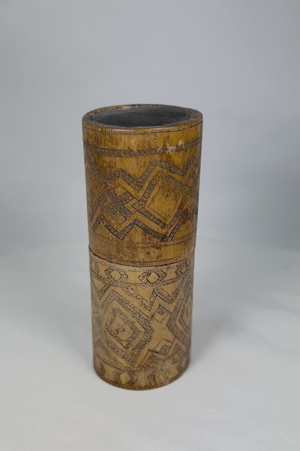 Antique carved bamboo container from Island Southeast Asia, 19th century, cylindrical with fitted lid and base, decorated with incised geometric patterns darkened with pigment, traditionally used for betel nut lime storage, photographed on a white background.