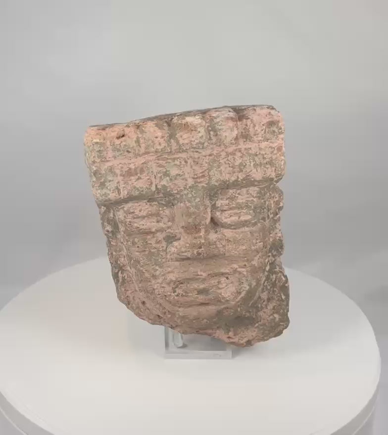 Rotating view of an ancient Veracruz ceremonial stone head hacha from Mexico, dating circa 600–900 CE, with a carved face, stepped headdress, weathered surface, and surviving pinkish-red deposits.