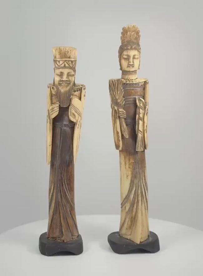 Rotating video of a matched pair of vintage Chinese carved-bone Emperor and Empress figurines, mid-to-late 20th century, featuring elaborate headdresses, expressive facial details, flowing imperial-style robes, decorative accessories, contrasting cream and dark-brown surfaces, and individual black display bases.