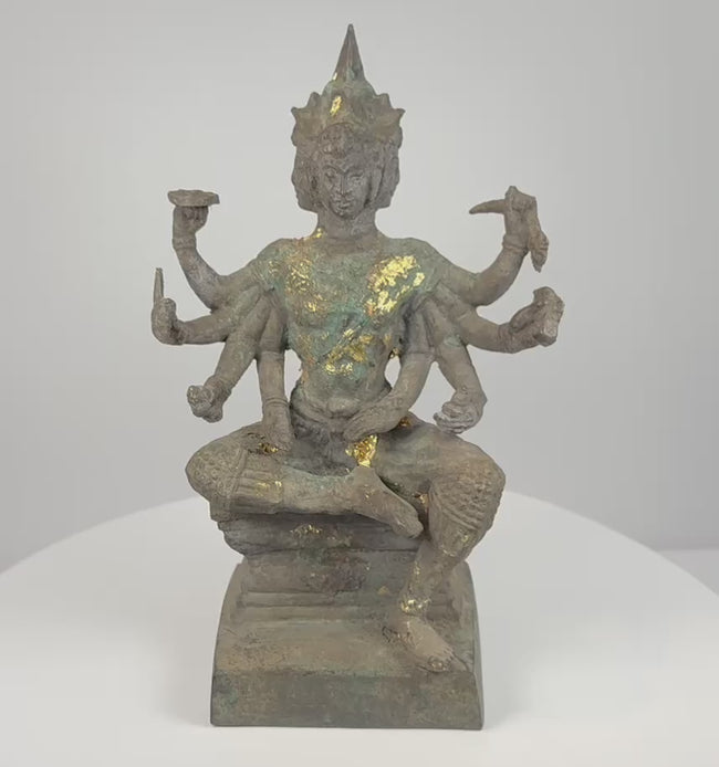 360-degree video of an antique Thai Phra Phrom bronze statue showing its four faces, eight arms, ritual attributes, gold leaf, aged patina, pedestal, and inscribed underside