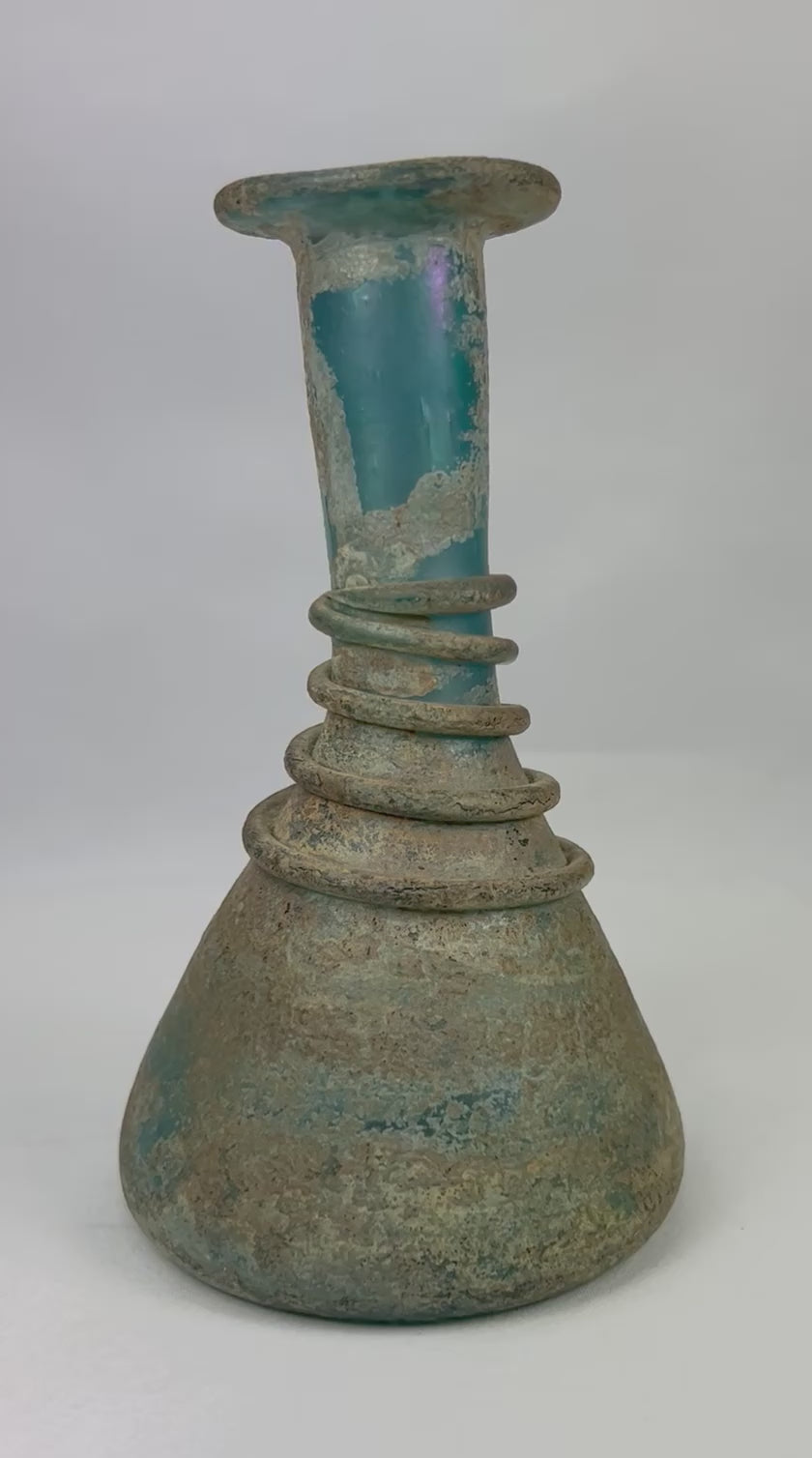 360-degree view of an ancient Roman turquoise glass unguentarium showing spiral trailing, elegant neck, flared rim, and mineral patina from centuries of burial