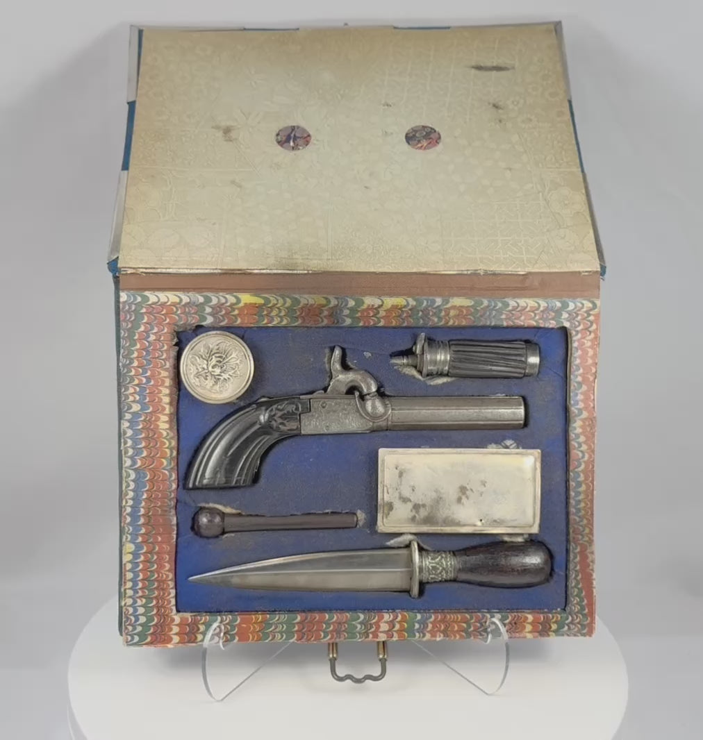 Video showing a rare 19th-century Continental European concealed defense set housed in a velvet-covered faux-book case, featuring an engraved percussion pistol, double-edged dagger, carved powder flask, loading rod, ammunition containers, and fitted accessories.