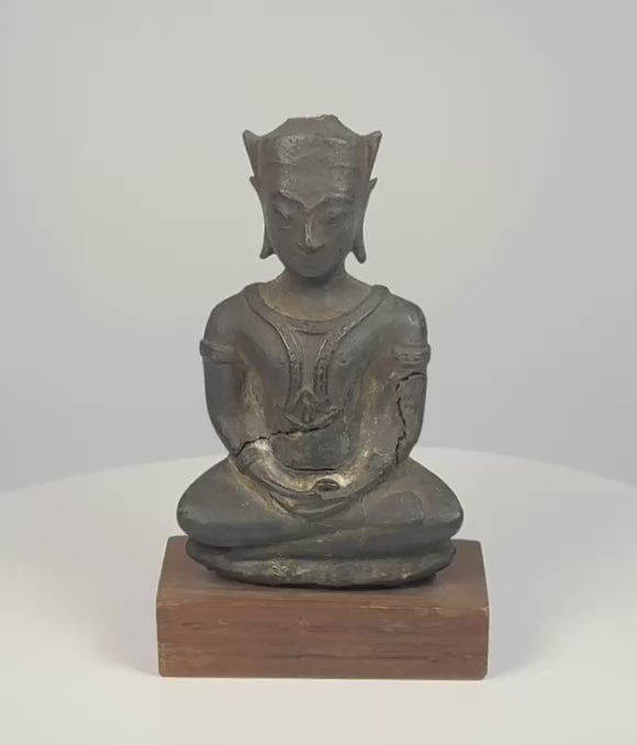 Video of a crowned bronze Buddha seated in meditation, with winged ear ornaments, dark patina, and a wooden display base.