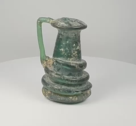 Video showcasing a Late Roman blue-green blown-glass jug with applied coiled trail decoration, iridescent surface, flared rim, and ancient burial patina