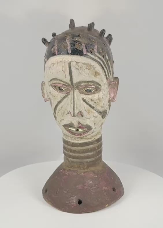 Rotating view of a Nigerian Igbo Janus dance crest featuring opposing carved human faces, original white, black, red, and purple pigments, projecting coiffure elements, a ringed neck, and a perforated base associated with ceremonial masquerade traditions of the mid-20th century.