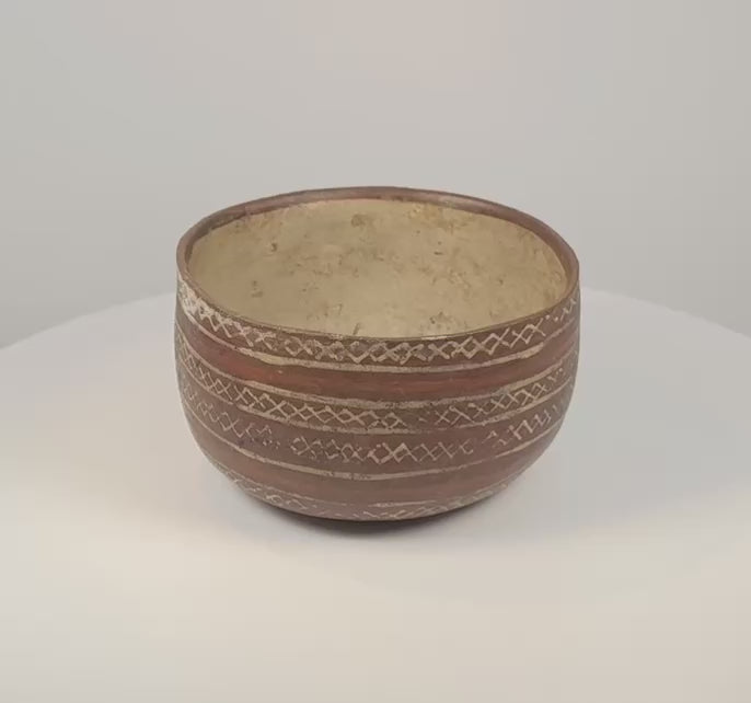 Rotating red-brown ceramic bowl showing cream X-shaped and diamond patterns, horizontal decorative bands and a pale buff interior.