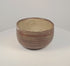 Rotating red-brown ceramic bowl showing cream X-shaped and diamond patterns, horizontal decorative bands and a pale buff interior.