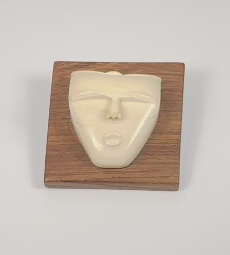 Rotating view of a mid-20th century hand-carved animal bone spirit face sculpture mounted on a polished hardwood plaque, highlighting its minimalist facial features, natural patina, and tribal-inspired modernist design.