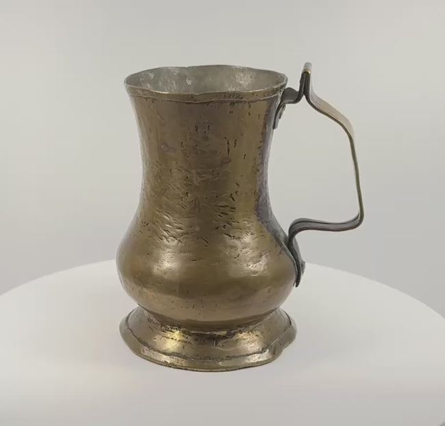 Rotating 360-degree presentation of an 18th-century George II English brass baluster tankard, showing its handle, flared rim, footed base, and aged patina.