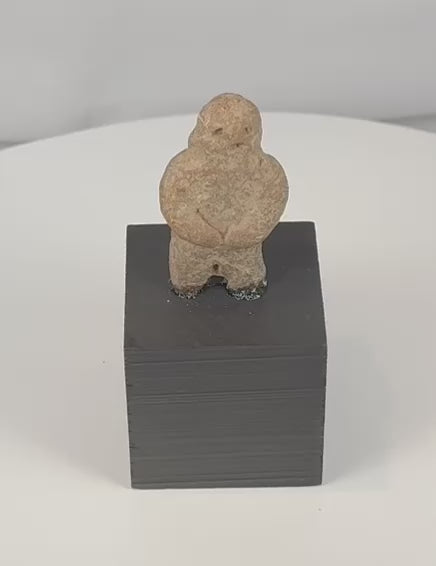 Rotating view of a Pre-Columbian carved stone standing figure with folded arms, deeply recessed eyes, compact proportions, weathered surfaces, mineral deposits, and a custom display stand