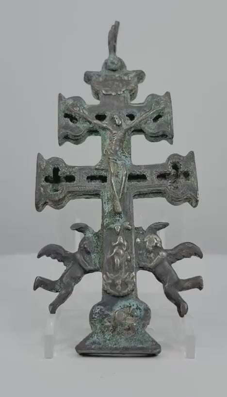 360-degree rotating view of an antique Spanish Caravaca bronze crucifix pendant, attributed to the 17th century. Features a double-barred cross with the crucified Christ, two winged angels, intricate religious imagery on both sides, traces of historic silvering, and a richly aged green and brown patina.