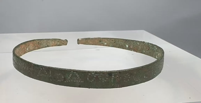 Rotating view of an ancient Western Asiatic penannular bronze bracelet with a flat-section band, stylized animal-head terminals, incised hatched decoration, pointillé triangles, annulet motifs, tapered ends, and green, blue-green, brown, and earthen archaeological patination