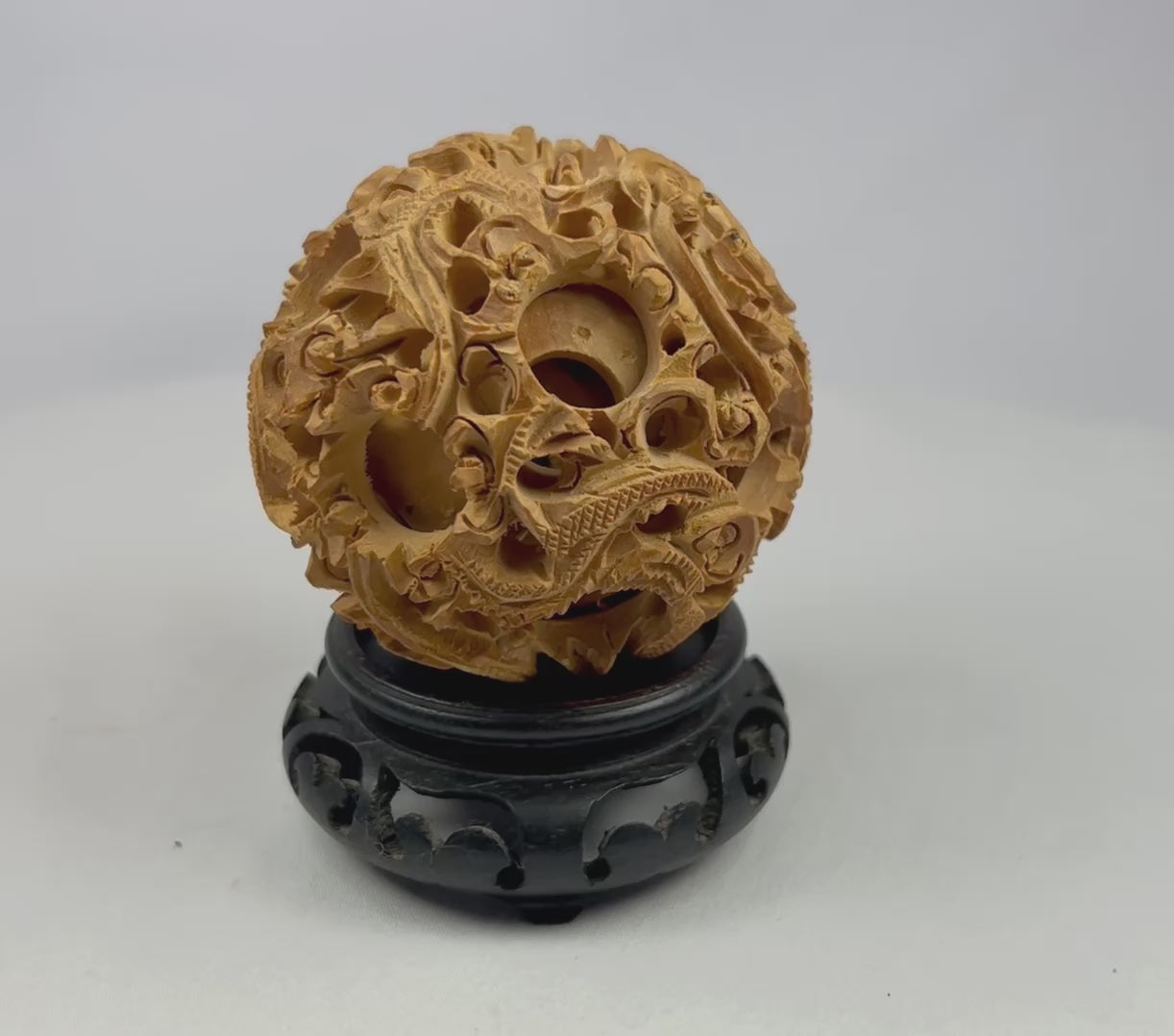 Ancient Chinese multi-layer carved puzzle ball with dragons displayed on a black carved stand against a white background.