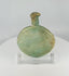360-degree view of an ancient Roman free-blown pale green glass flask with flattened circular body, elongated neck, burial encrustation, iridescence, and historic repairs displayed on a clear acrylic stand.