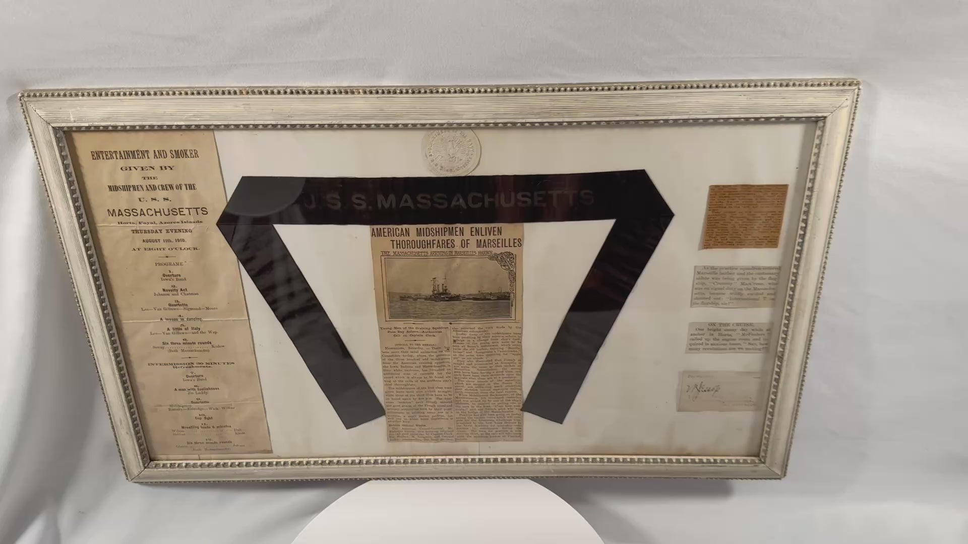Zoomed in video of a framed USS Massachusetts (BB-2) naval archive featuring an original silk hatband ribbon, 1910 Mediterranean cruise ephemera, newspaper clippings, embossed seal, and historical U.S. Navy memorabilia from the battleship's final years of service.