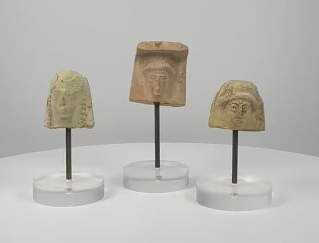 360° rotating video showcasing a set of three ancient Greek terracotta female protomai bust plaques, dating to the 6th–4th century BCE. Each fragment features distinct facial details, hairstyles, and headdresses, with natural patina and age-related wear. Individually mounted on clear acrylic display stands.
