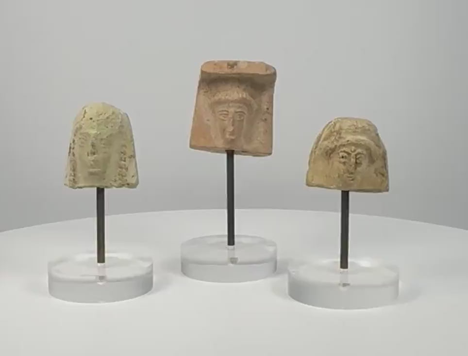 360° rotating video showcasing a set of three ancient Greek terracotta female protomai bust plaques, dating to the 6th–4th century BCE. Each fragment features distinct facial details, hairstyles, and headdresses, with natural patina and age-related wear. Individually mounted on clear acrylic display stands. 