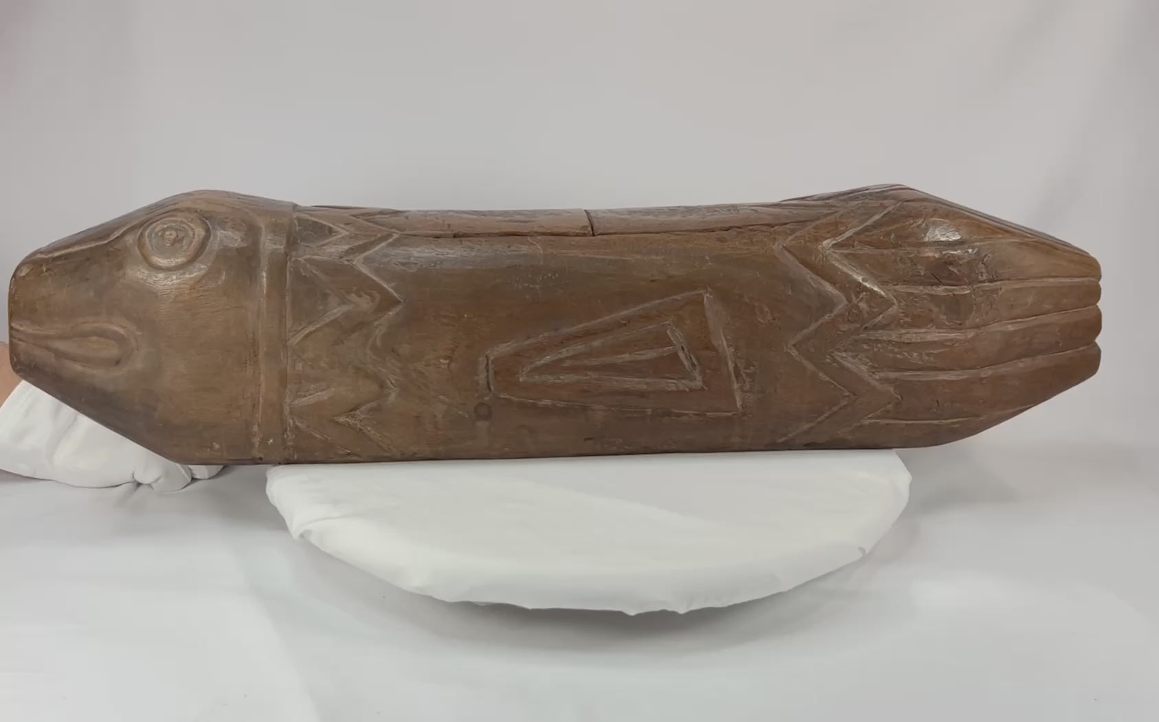 360-degree rotation of a hand-carved Melanesian wooden fish drum from the 19th–20th century, showing incised patterns, hollow body, and detailed head carvings.
