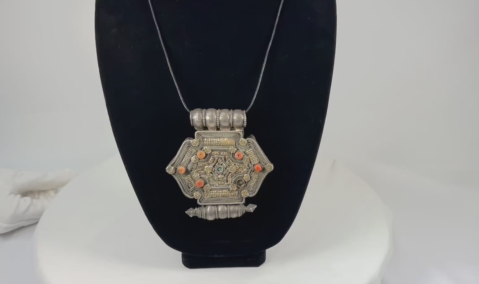 Hexagonal Himalayan gau (ghau) amulet pendant in silver-tone alloy with parcel-gilt filigree, rosette appliqués, inset coral beads, and small turquoise cabochon, featuring hollow reliquary cavity and tubular suspension bales, late 19th–early 20th century, Tibet/Nepal