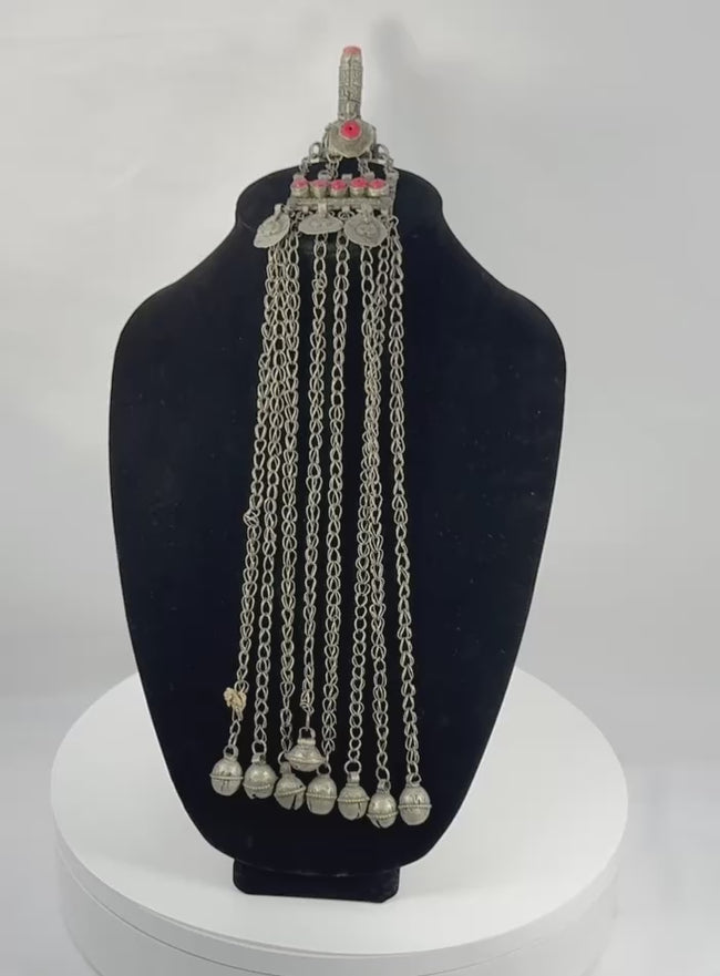 Antique Afghan Kuchi tribal pendant featuring a cylindrical hirz prayer tube, red glass cabochons, silver-toned metalwork, cascading chain tassels, and bell-shaped pendants, showcasing traditional nomadic ceremonial craftsmanship from the late 19th to early 20th century.