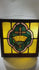 Early 20th-century stained glass panel, 16x16 in., with central cross and crown motif in amber, green, and pink, set in a wooden frame.