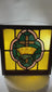 Early 20th-century stained glass panel, 16x16 in., with central cross and crown motif in amber, green, and pink, set in a wooden frame.