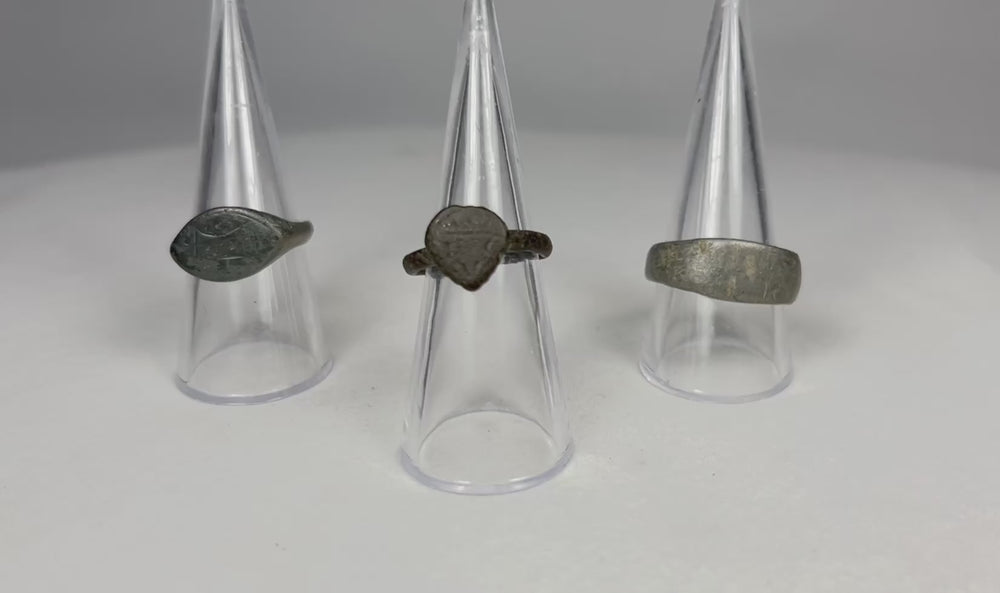 Rotating view of three authentic ancient European bronze rings, showing engraved oval signet ring, medieval heart or shield bezel ring, and heavy bronze band with rich aged patina.
