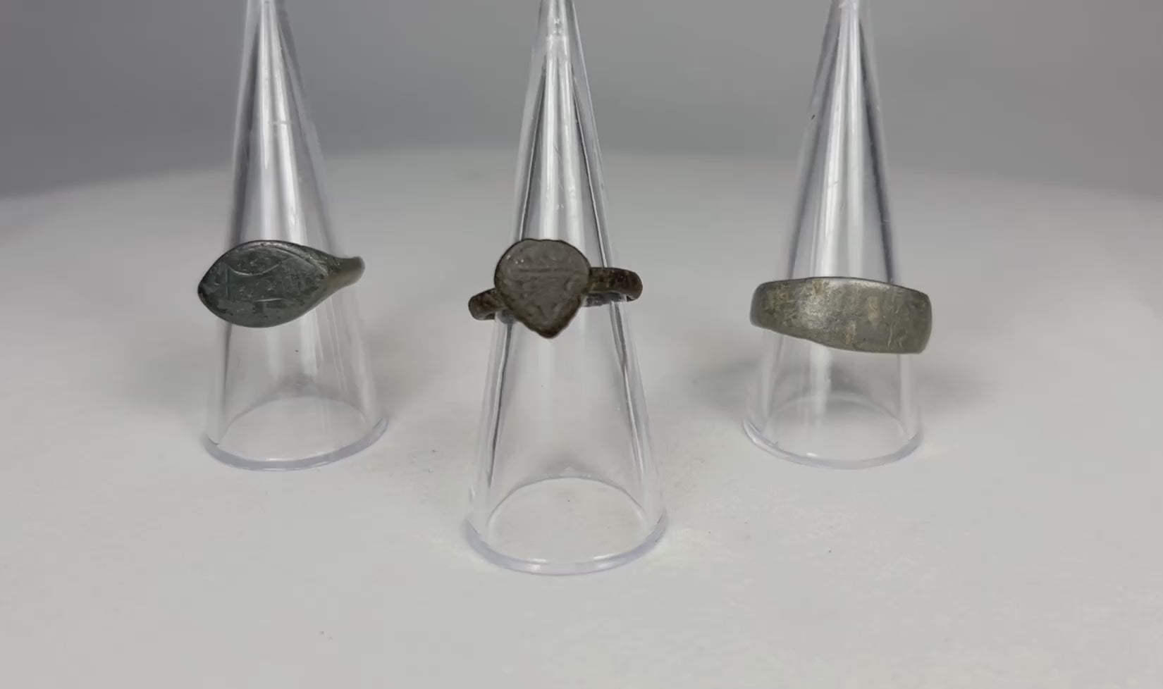 Rotating view of three authentic ancient European bronze rings, showing engraved oval signet ring, medieval heart or shield bezel ring, and heavy bronze band with rich aged patina.
