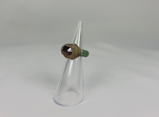 360-degree view of an ancient Neo-Assyrian bronze ring featuring a deep red garnet intaglio and natural green patina, rotating on a display stand.