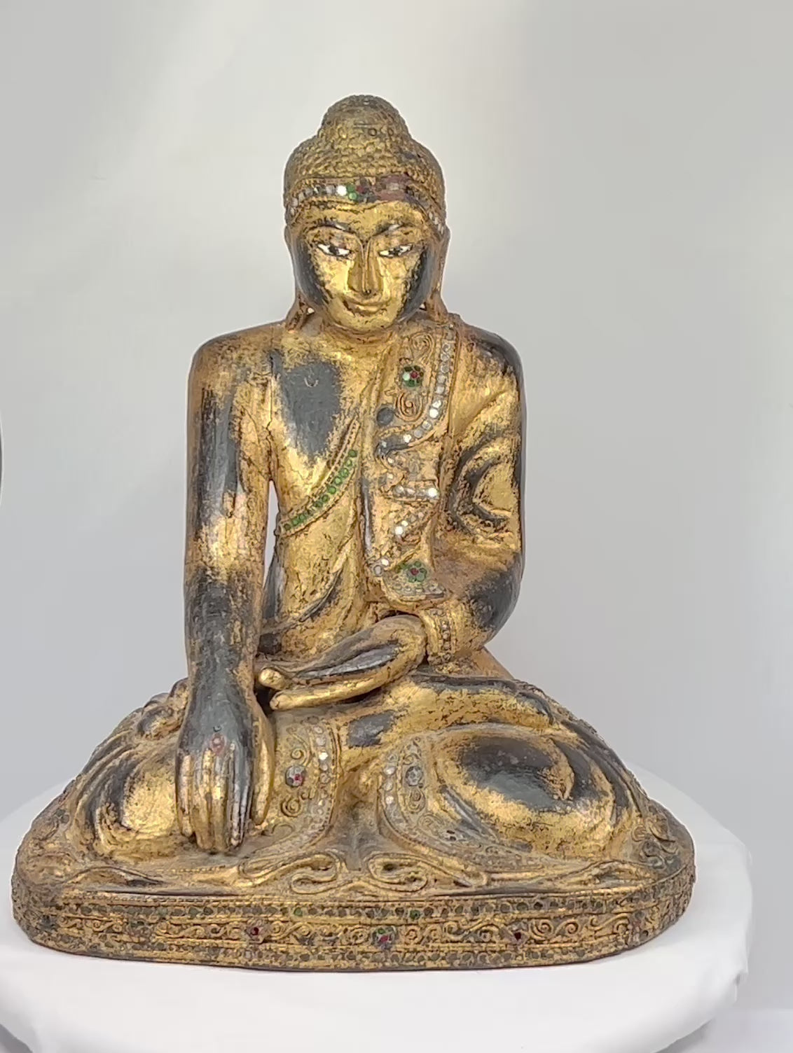 Hand-carved wooden Thai Buddha statue with gilt paint and colorful glass inlays, seated in Bhumisparsha Mudra, symbolizing enlightenment, circa 19th–early 20th century.