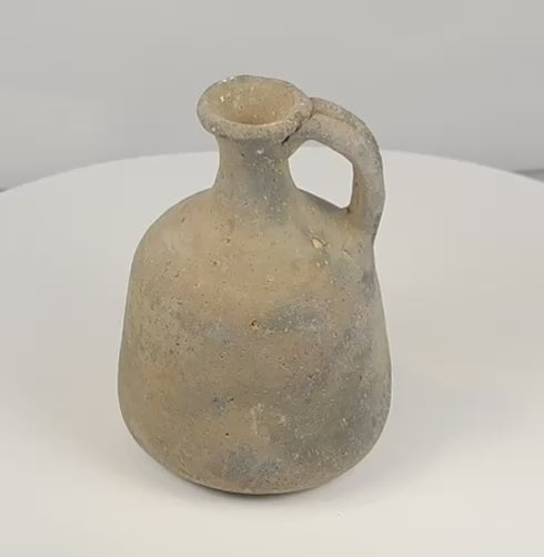 Rotating view of an ancient Iron Age Eastern Mediterranean or Levantine grey-fired earthenware jug with a rounded ovoid body, narrow cylindrical neck, thick flared rim, broad loop handle, mineral inclusions, firing pits, and an undecorated utilitarian surface