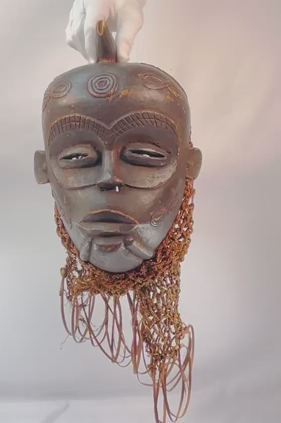 Chokwe wooden ceremonial mask from Central Africa with serene closed eyes, geometric forehead motifs, and wickerwork fiber adornments, 19th–20th century CE.