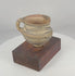 360-degree rotating view of an ancient Chinese painted pottery vessel from Northwest China, featuring black geometric decoration, traces of red pigment, a single strap handle, raised ring foot, archaeological weathering, and a custom hardwood display stand.