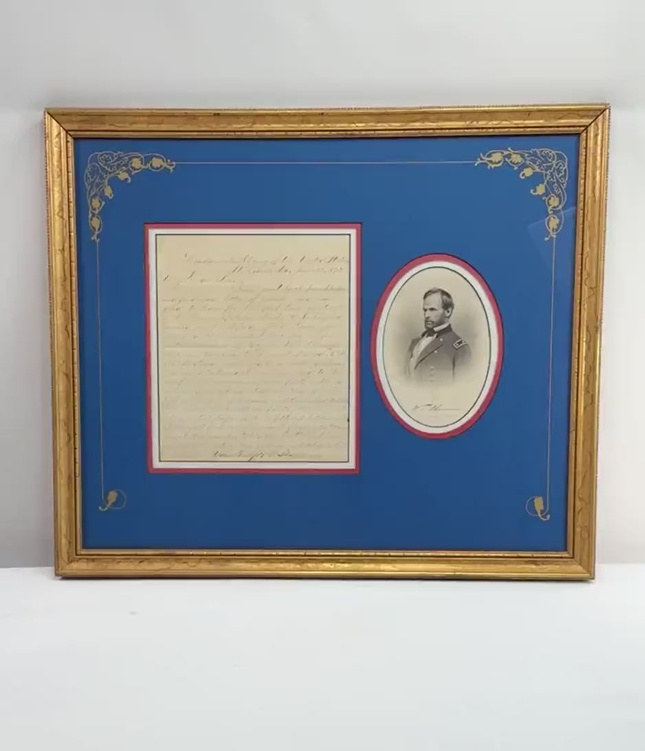 Video showcasing a framed historical presentation featuring a reproduction of an 1875 letter attributed to Civil War General William Tecumseh Sherman alongside an engraved portrait in military uniform. The display features royal-blue matting, decorative gold floral accents, red and white borders, and an ornate gilt-finished frame.