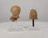 360-degree rotating view of two ancient terracotta female votive head fragments, circa 6th–4th century BCE. Features an Etruscan female head with a rounded veil and an East Greek protome with intricately patterned hair and stylized facial features. Both artifacts are displayed on individual clear acrylic stands, revealing their sculptural details, surface textures, and age-related wear.