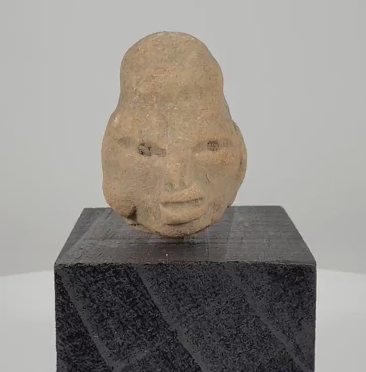 Ancient Pre-Columbian terracotta head fragment from West Mexico, circa 300 BCE–300 CE, featuring an elongated cranium, almond-shaped eyes, prominent lips, weathered clay surface, and custom black display stand.