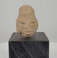 Ancient Pre-Columbian terracotta head fragment from West Mexico, circa 300 BCE–300 CE, featuring an elongated cranium, almond-shaped eyes, prominent lips, weathered clay surface, and custom black display stand.