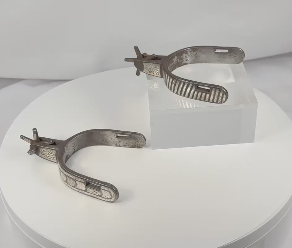Rotating view of a pair of antique Western steel spurs with engraved silver inlay, broad heel bands, five-point rowels, and aged patina