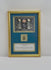 Video of a framed ancient Egyptian-style blue-green glazed scarab amulet, attributed to circa 2345–30 BCE, mounted within a gold-toned display against a deep blue background. The gilt frame features Egyptian-inspired artwork depicting a sacred scarab, solar disk, and winged figures, with an accompanying historical identification plaque.